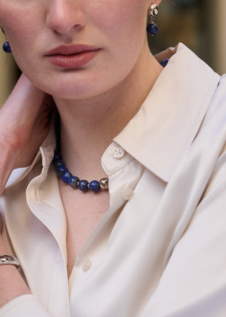 Woman wearing a white shirt with a blue beaded necklace and earrings.