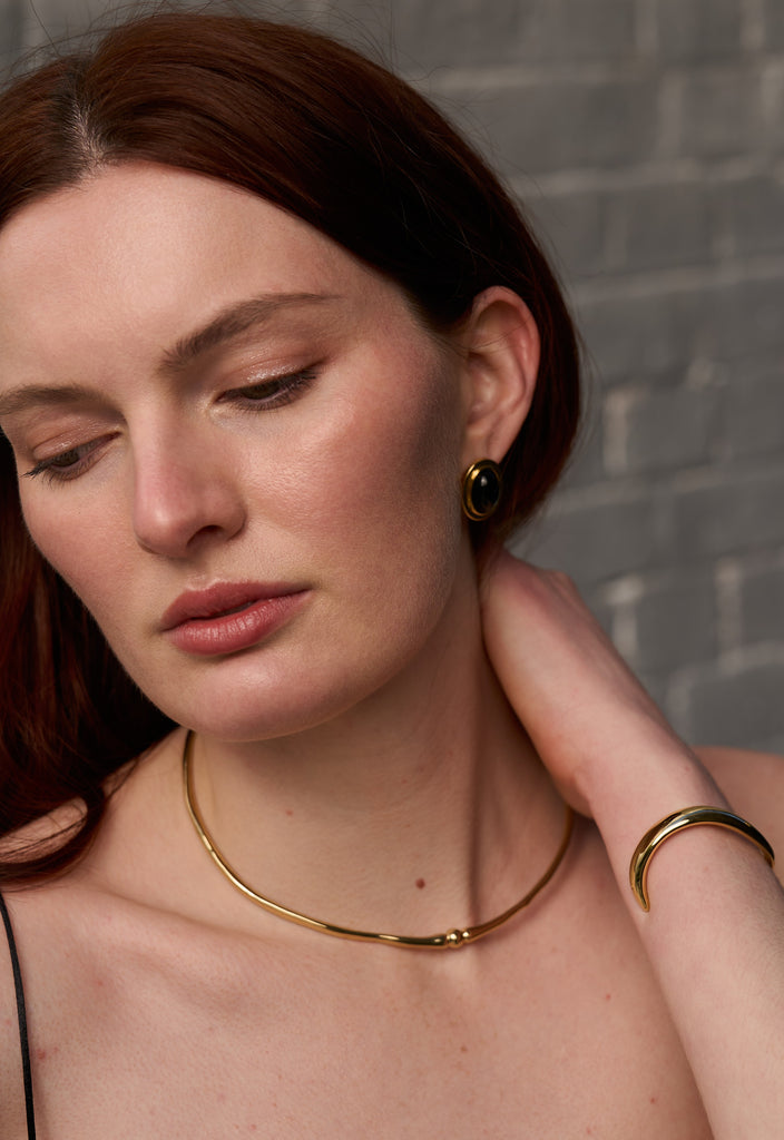 Woman wearing a gold necklace and earrings with a neutral background