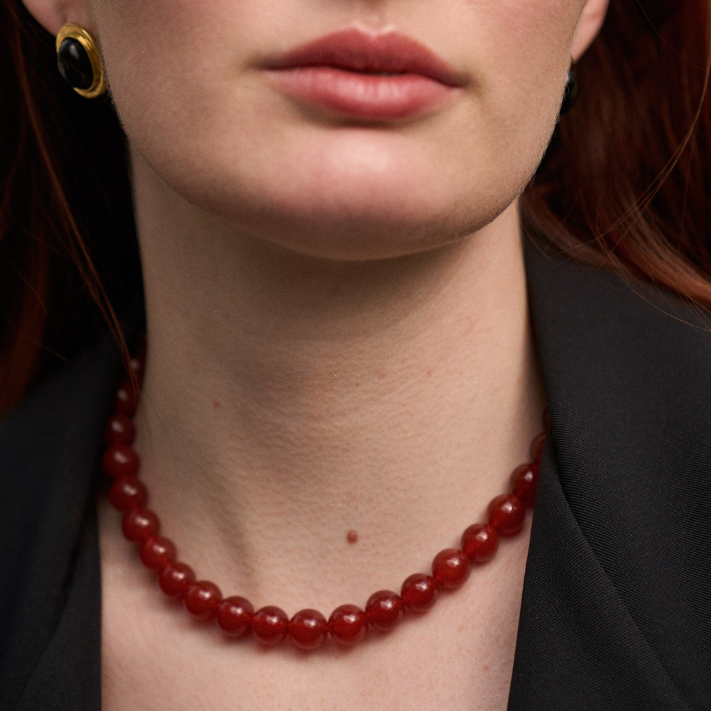Close-up of a person wearing a red beaded necklace with a blurred background