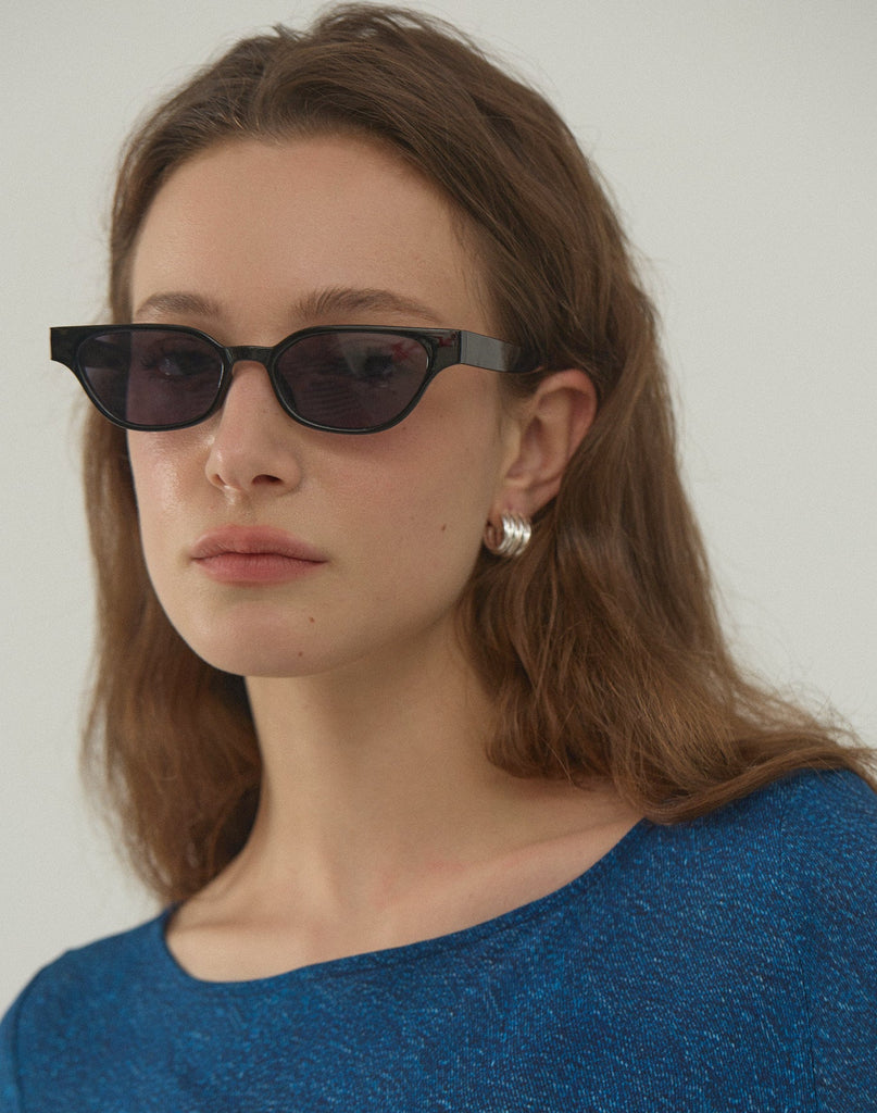Woman wearing dark sunglasses and a blue top against a plain background