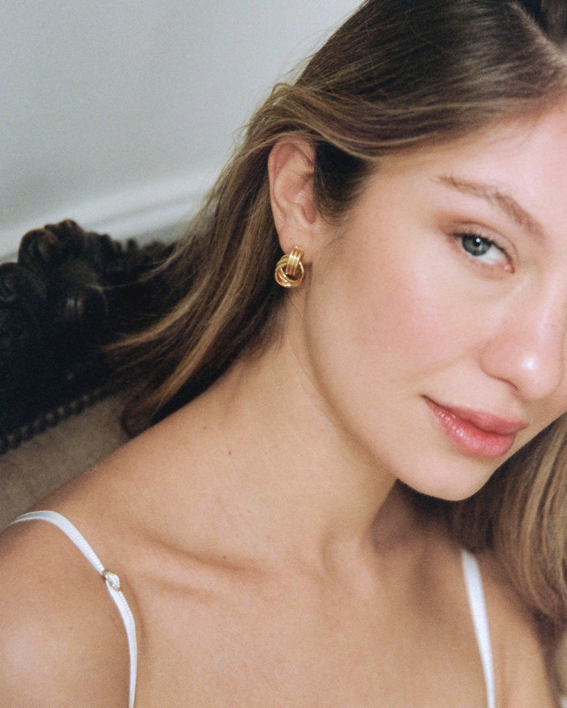 Close-up of a woman wearing gold hoop earrings with a neutral background