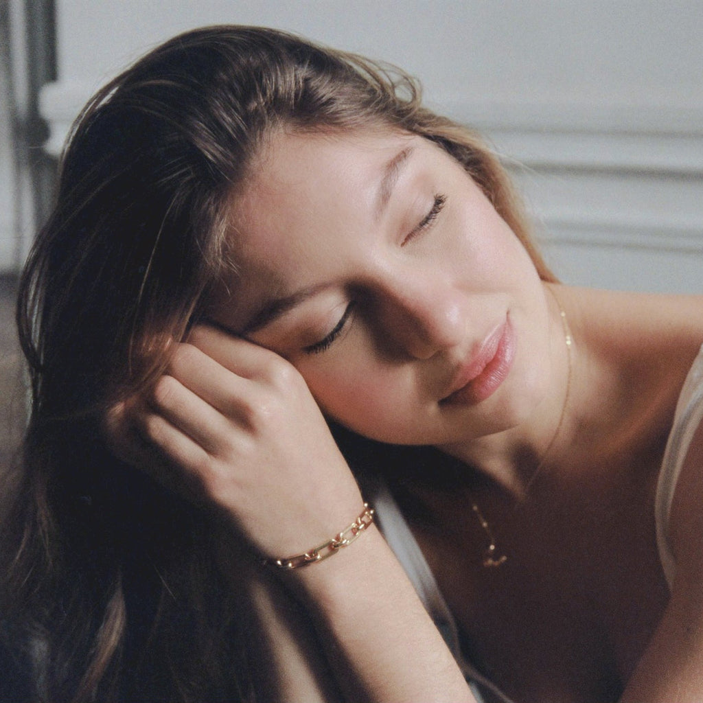 Woman with closed eyes resting her head on her hand, wearing a white tank top.