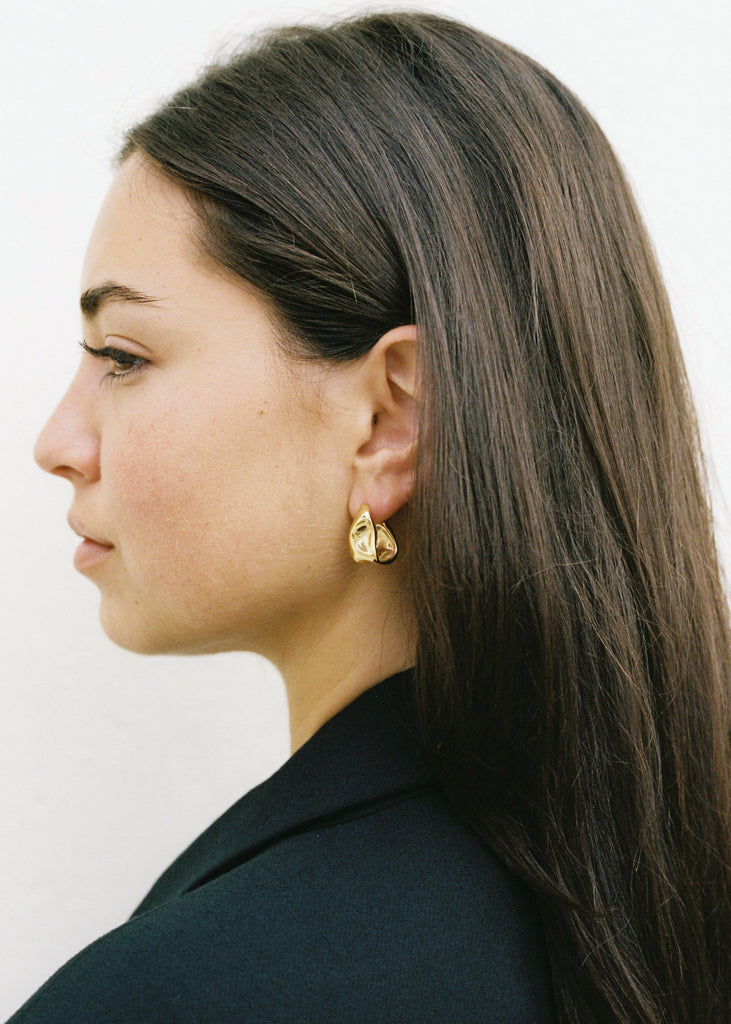 Woman wearing gold earrings with a plain background