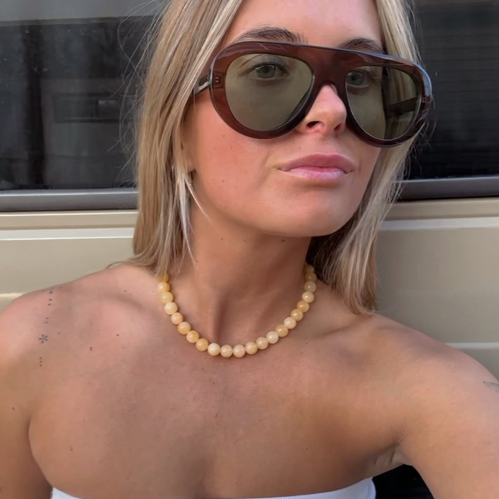 Woman wearing sunglasses and a white top in front of a beige vehicle