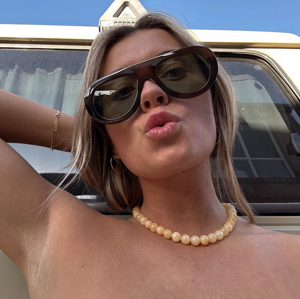 Woman wearing sunglasses and a pearl necklace in front of a vehicle