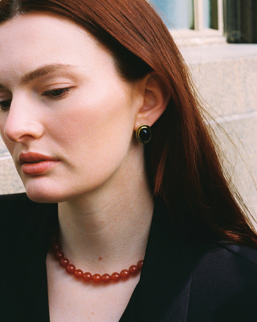 Woman wearing a red necklace and black earrings against a neutral background