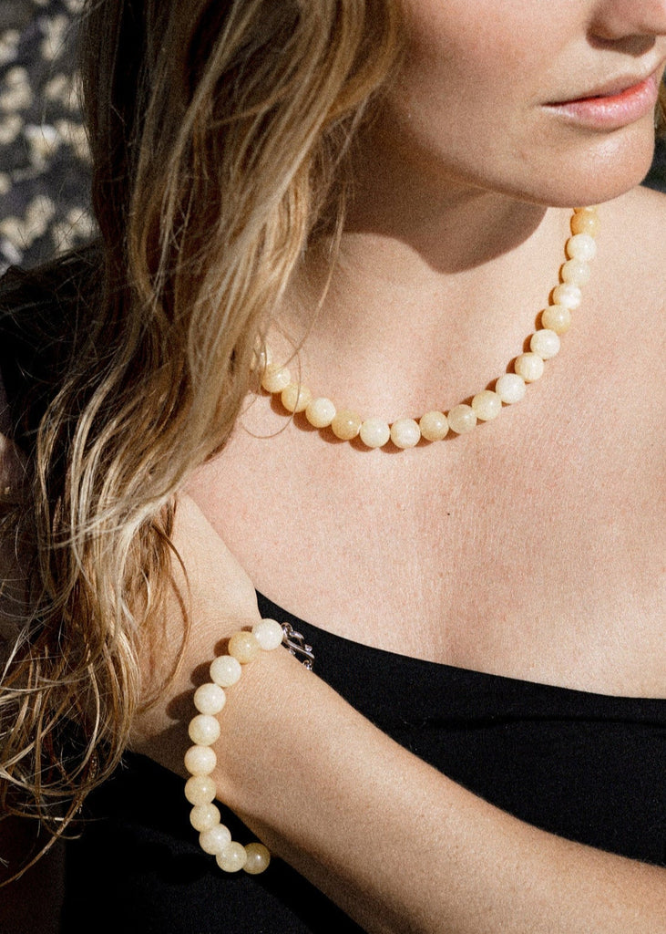 Woman wearing a beige beaded necklace against a textured wall.