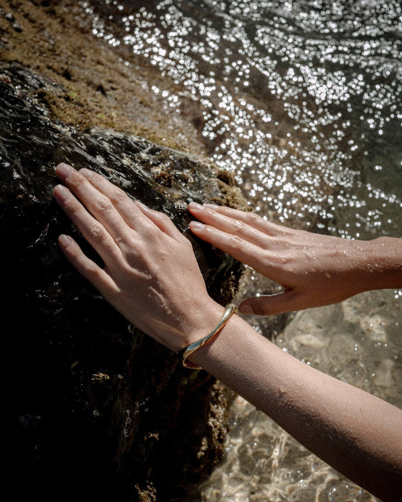 Hands touching a rock with water in the background